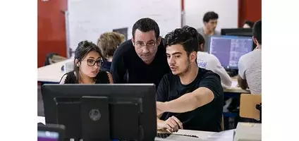 Une jeune fille et un jeune homme devant un ordinateur avec un enseignant